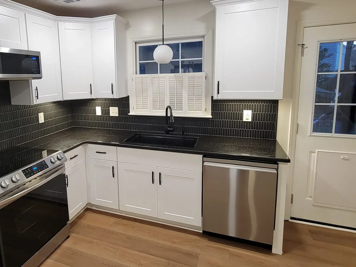 Modern white cabinets with high-end appliances, overhang lighting, and black tile backsplash
