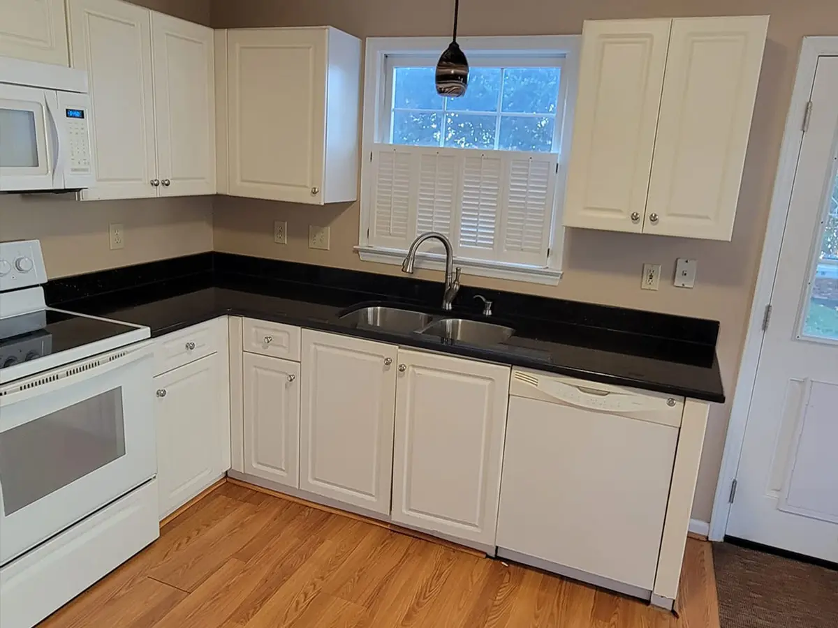White kitchen cabinets with black countertop and no backsplash with white appliances