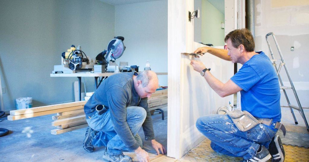 Two workers installing a door frame inside a home under renovation.