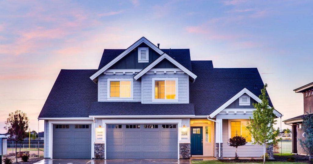 A two-story home with blue siding, a garage, and glowing interior lights at dusk.