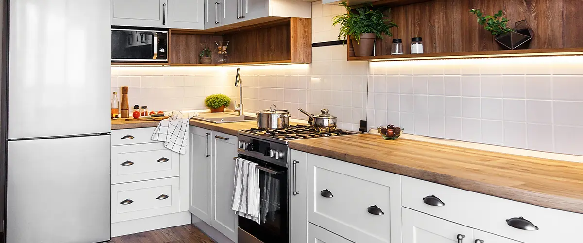 Contemporary small kitchen with white cabinets, wood countertops, under-cabinet lighting, and stainless steel appliances.