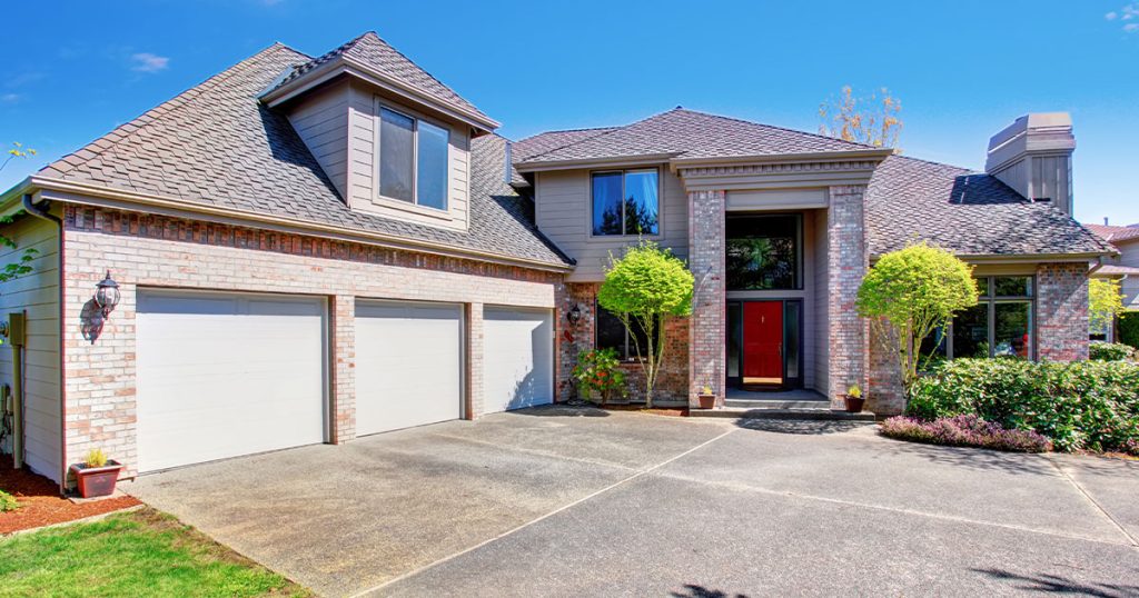 Modern suburban house with three-car garage and concrete driveway surrounded by manicured landscaping