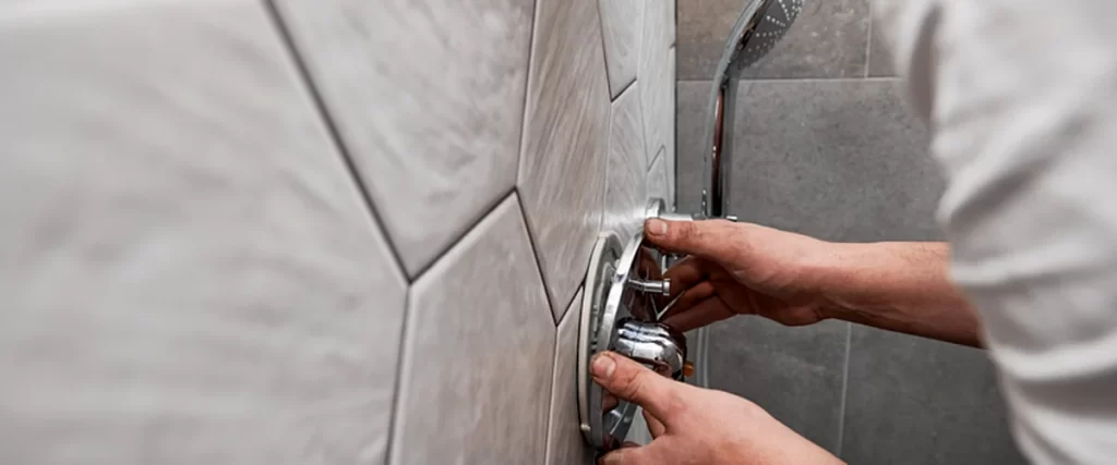 Contractor adjusting a modern chrome shower valve on a hexagonal tiled bathroom wall, highlighting expert plumbing installation and craftsmanship.