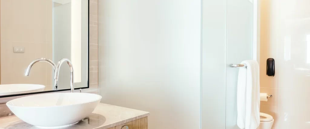 Shower insert vs tiled shower example featuring a frosted glass shower enclosure, white ceramic vessel sink, chrome faucet, and wood vanity with expert craftsmanship